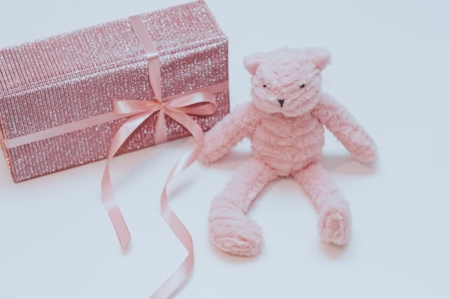 Get Registry Results: Tips to Enhance Your Gift Registry Service, a present wrapped in sparkly pink wrapping paper, tied together with a pink ribbon, sitting to the left of a pink plush bear.