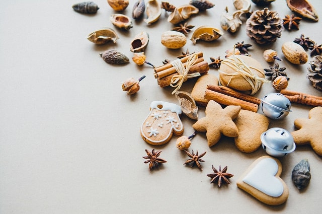 Holiday Gifting: Start Marketing Your Holiday Wish List Now, a pile of pinecones, holiday themes sugar cookies, and some Christmas bells on a table.