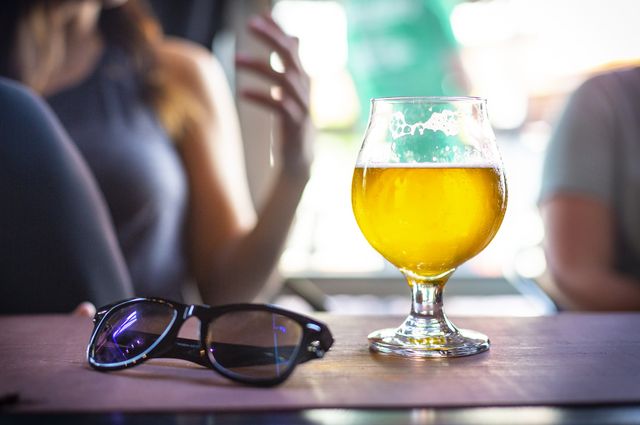 People at a table with a glass filled with beer and a pair of sunglasses.